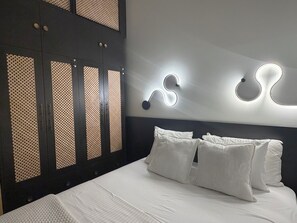 Une chambre à coucher avec un lit, des oreillers blancs, une tête de lit sombre et une armoire dont les portes sont ornées de motifs.