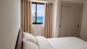 A bedroom with a bed, curtains, a window, and a view of the sea. - Modern Ocean View Oasis, Pool & Free Parking (Santo Domingo Este)