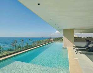 A swimming pool with a view of the ocean, lounge chairs, and a clear sky. - Modern Ocean View Oasis, Pool & Free Parking (Santo Domingo Este)