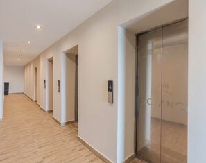 A modern hotel corridor with a wooden floor, a glass elevator, and a series of doors. - Modern Ocean View Oasis, Pool & Free Parking (Santo Domingo Este)