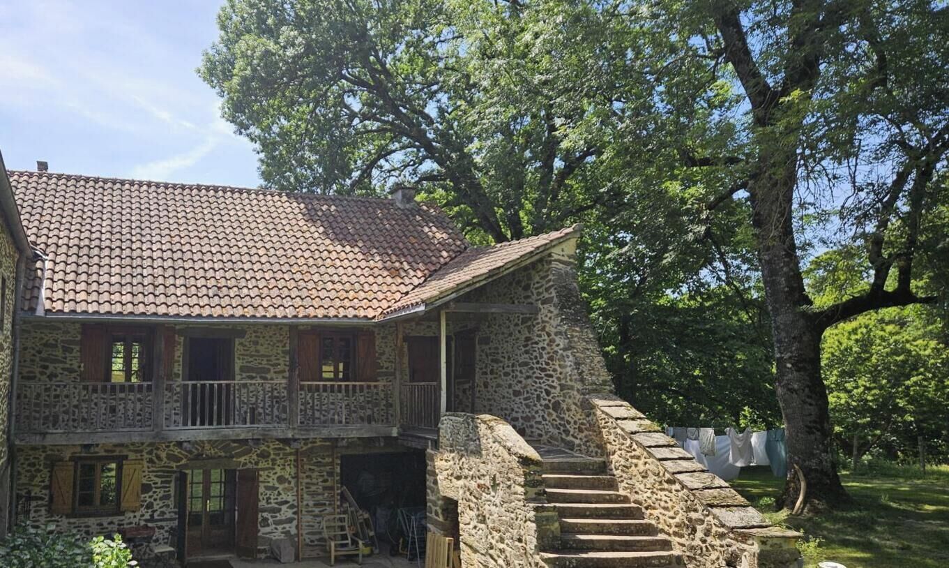 A stone building with a tiled roof, a balcony, and a staircase leading to a covered area.