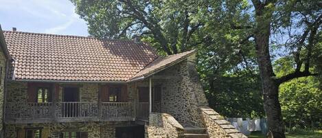 A stone building with a tiled roof, a balcony, and a staircase leading to a covered area.