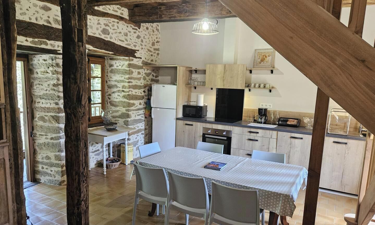 Een landelijke keuken met stenen muren, houten balken en een eettafel met stoelen.
