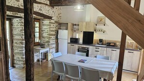 A rustic kitchen with stone walls, wooden beams, and a dining table with chairs. - La Viguerie - JOUQUEVIEL (JOUQUEVIEL)