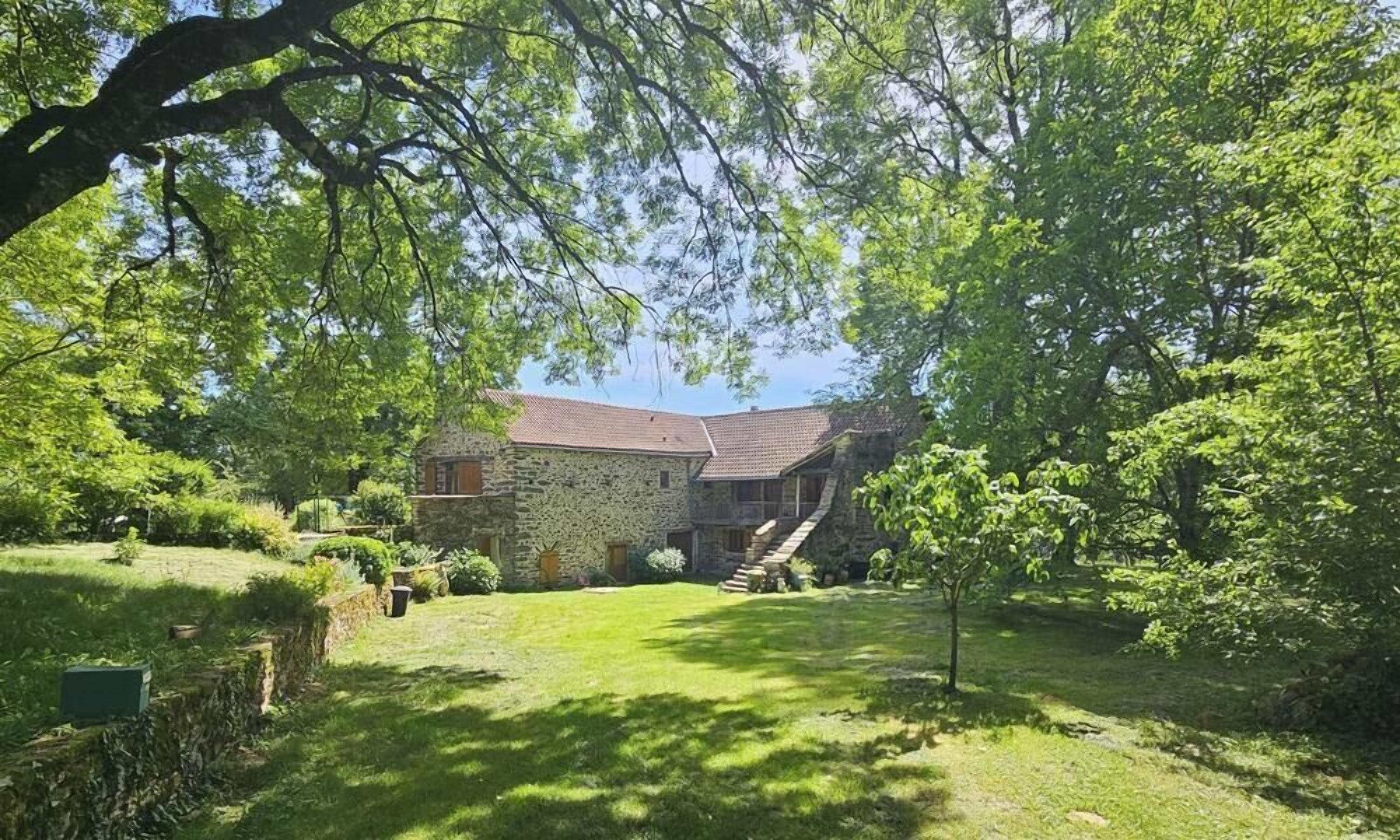 A stone house with a sloped roof, surrounded by a well-maintained lawn and trees.