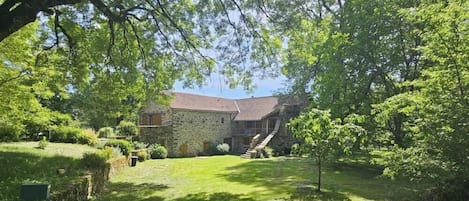 A stone house with a sloped roof, surrounded by a well-maintained lawn and trees.