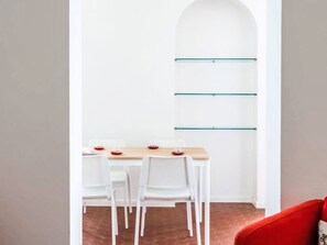 Ein Essbereich mit einem Holztisch, weißen Stühlen und einem roten Stuhl. Auf dem Tisch befinden sich drei rote Teller.