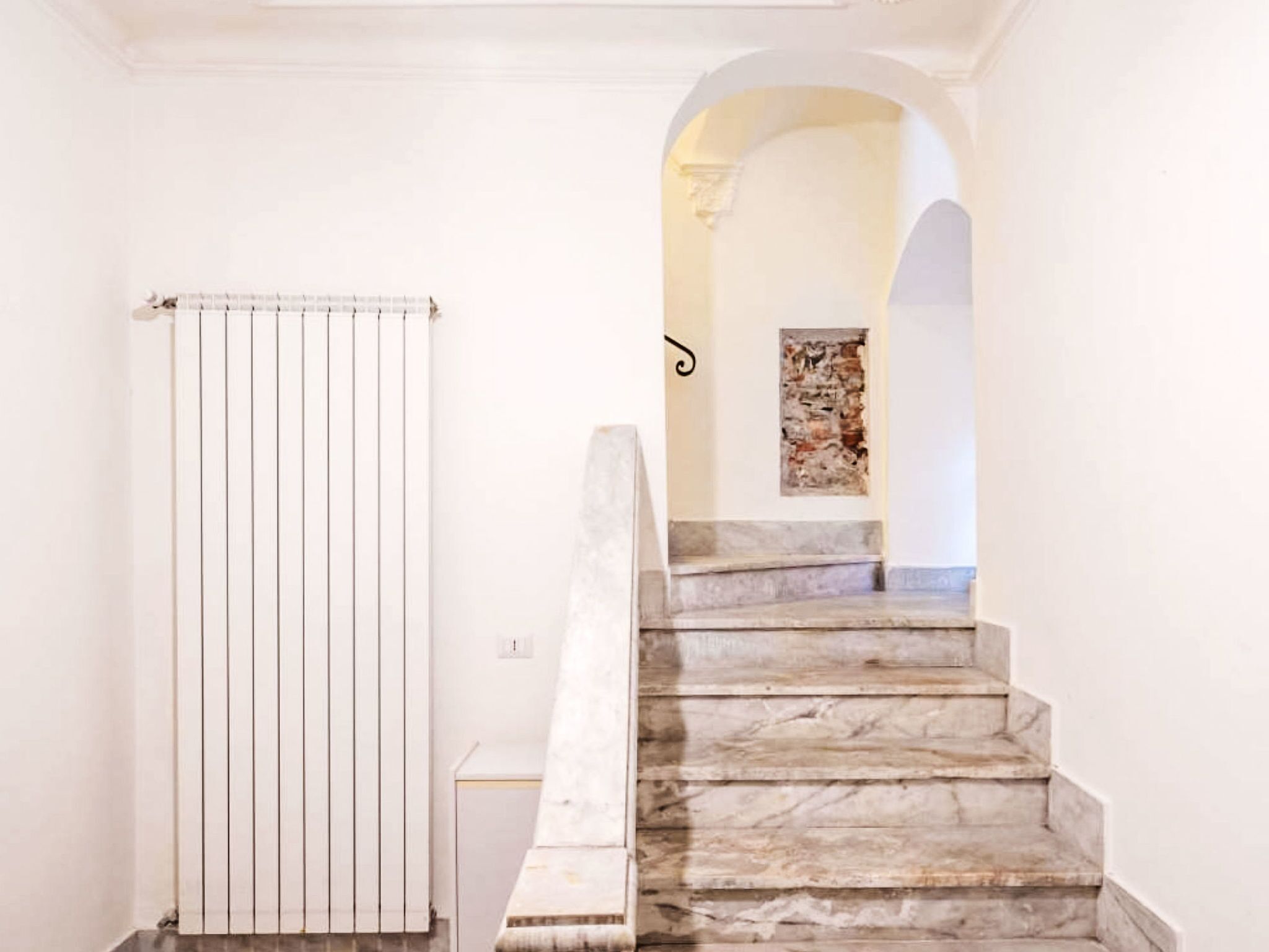 A staircase with marble steps leading to an upper floor, a white radiator, and a wall-mounted artwork.