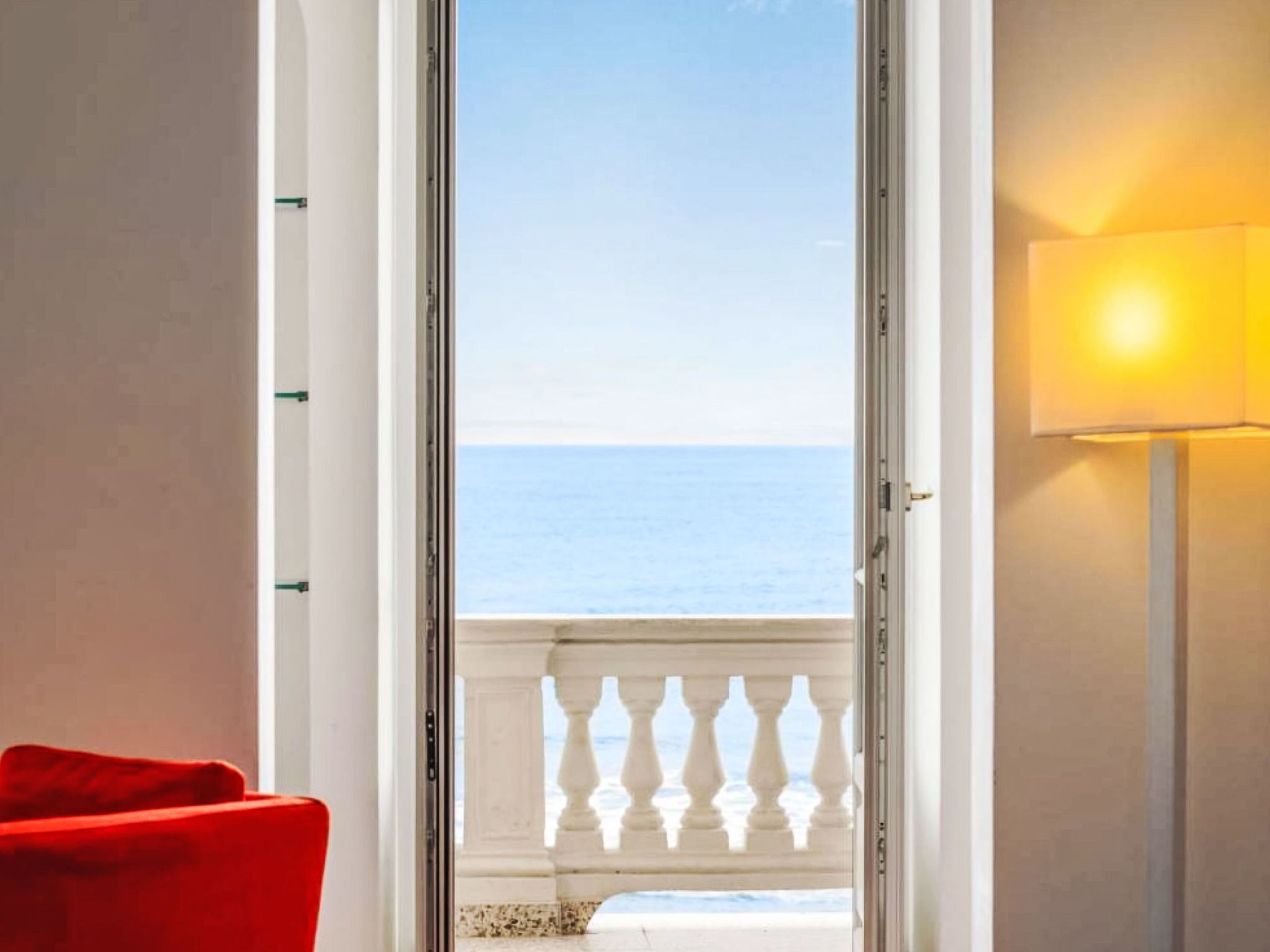 Een kamer met uitzicht op zee, te zien door een deur met een witte balustrade.
