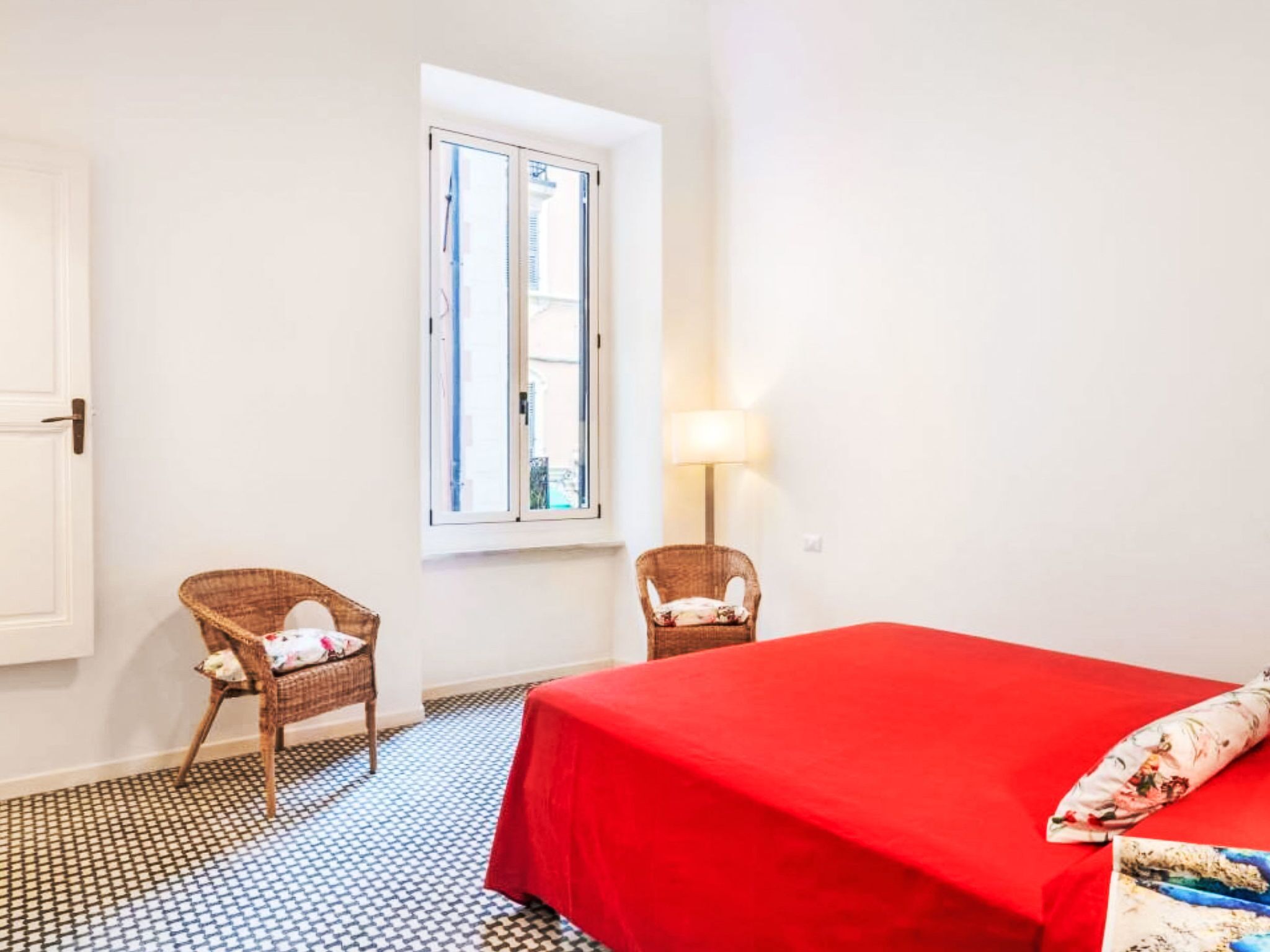 A room with a bed, two chairs, a window, and a lamp.