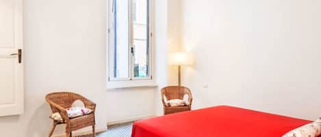 A room with a bed, two chairs, a window, and a lamp.