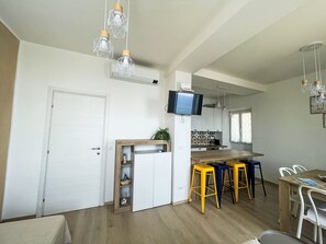 Et moderne køkken med indbygget TV, træbarstole og et spiseområde med hvide stole.