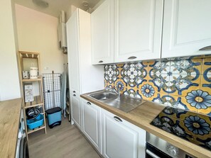 Una cocina compacta con gabinetes blancos, un lavamanos de acero inoxidable y un salpicadero con diseño.