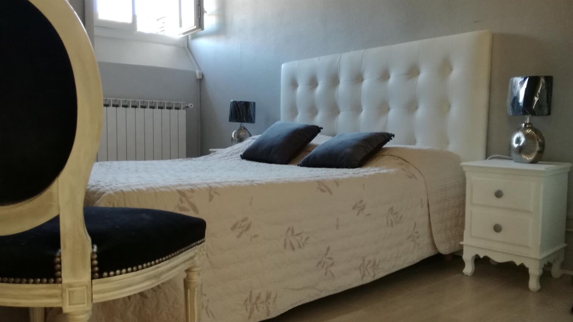 Een slaapkamer met een bed, een stoel, een nachtkastje en een lamp.