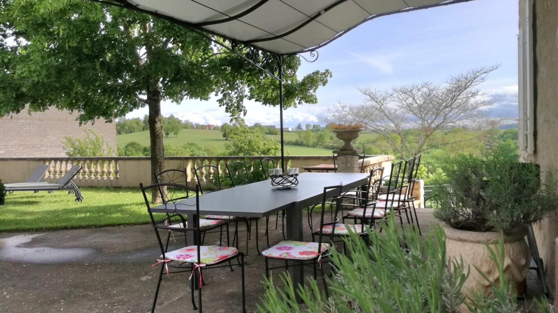 An outdoor patio with a table and chairs, a covered area, and a view of a green landscape.