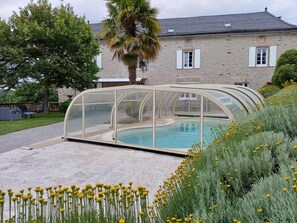 Ein Schwimmbecken mit Glasüberdachung, umgeben von einem Garten mit gelben Blumen und einer Palme.