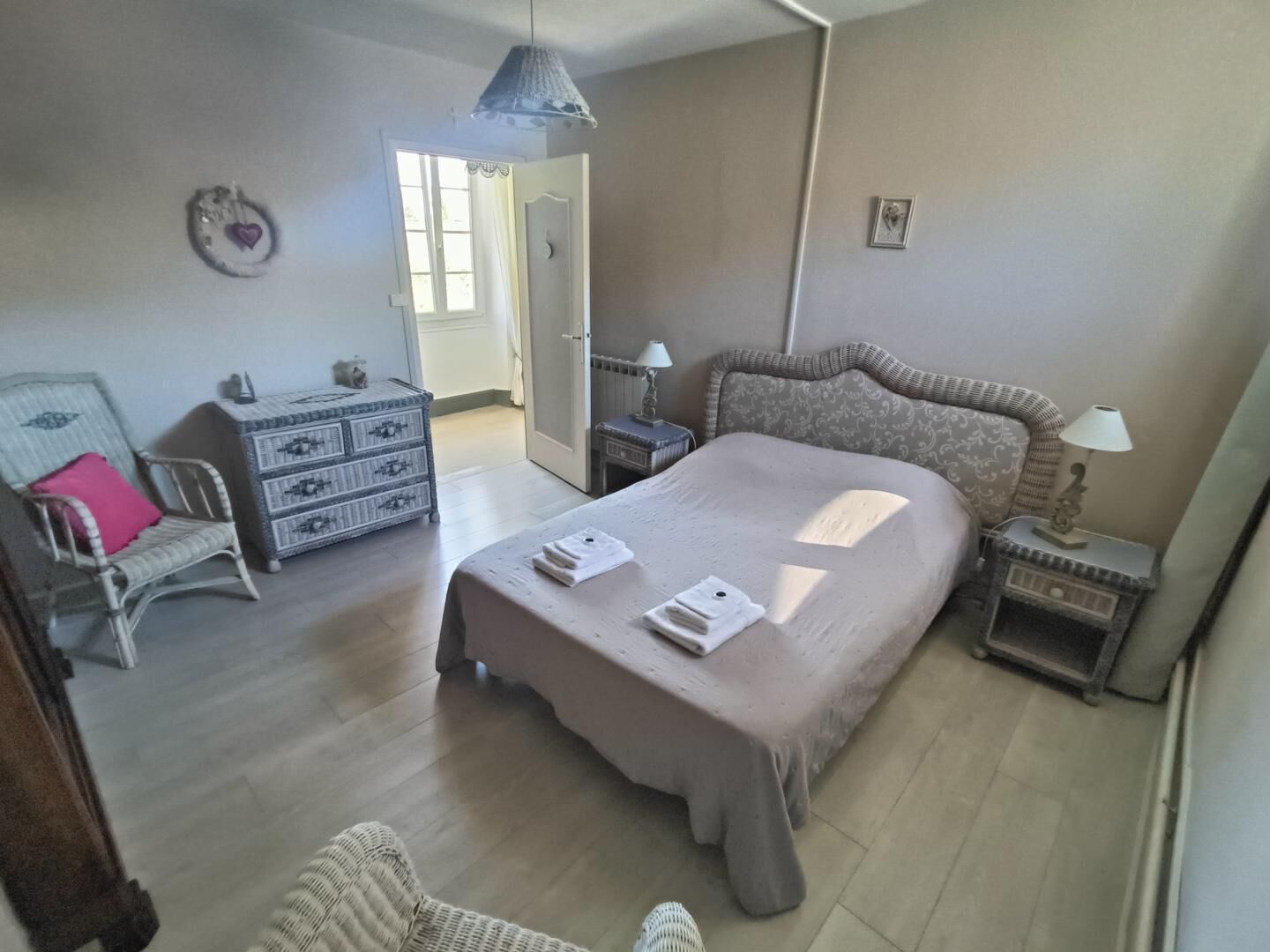 Een slaapkamer met een groot bed, een dressoir, een stoel en een nachtkastje met een lamp.