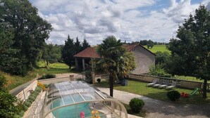 Una piscina con cerramiento de vidrio, rodeada por un jardín ajardinado y un edificio de ladrillo al fondo.