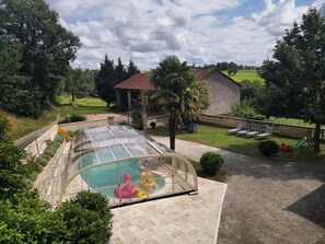Ein Schwimmbad mit Glasüberdachung, umgeben von einem angelegten Garten, mit einem Backsteinhaus im Hintergrund.