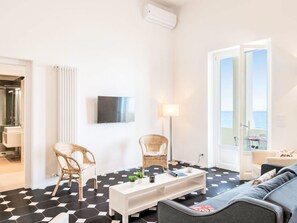 A modern living room with a black and white checkered floor, two wicker chairs, a white sofa, a coffee table, and a flat-screen TV mounted on the wall. - The Wharf by Interhome (Alassio)