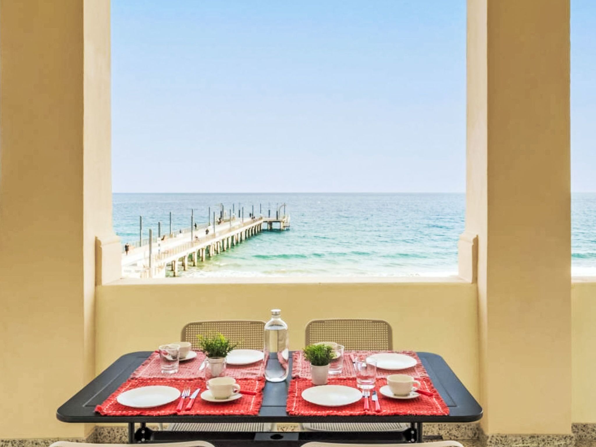 Une table dressée pour deux personnes, avec vue sur la mer et un quai.