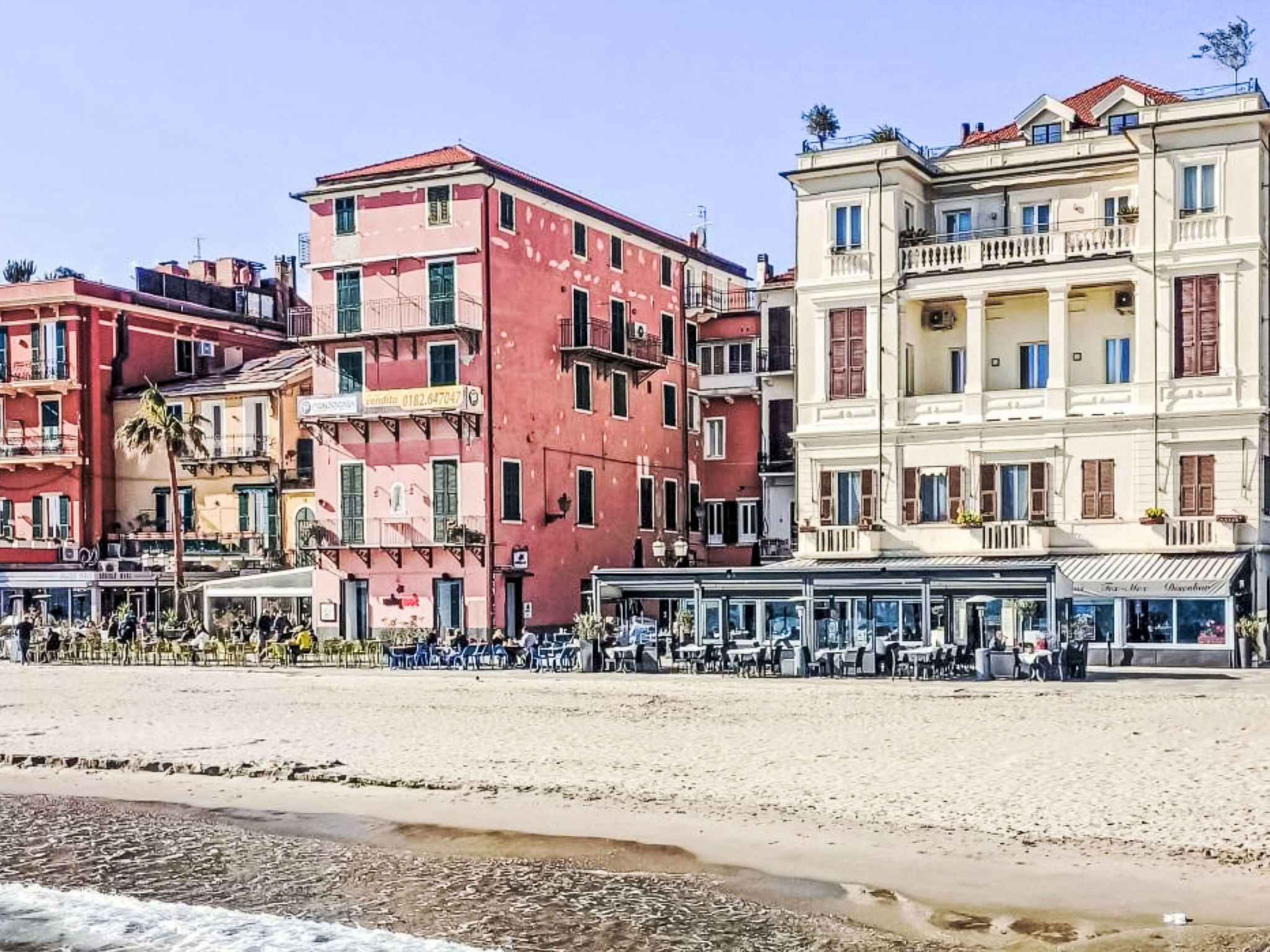 A beachfront with buildings, including a white building with balconies and a red building with a balcony.