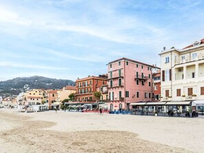 A coastal town with multi-story buildings, a sandy beach, and a mountain in the background. - The Wharf by Interhome (Alassio)