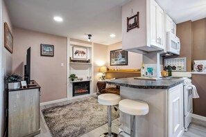 A modern kitchen with a central island, bar stools, a fireplace, and wall-mounted artwork. - Cozy Garden Retreat | Pet Friendly w/ Private Yard (Colorado Springs)