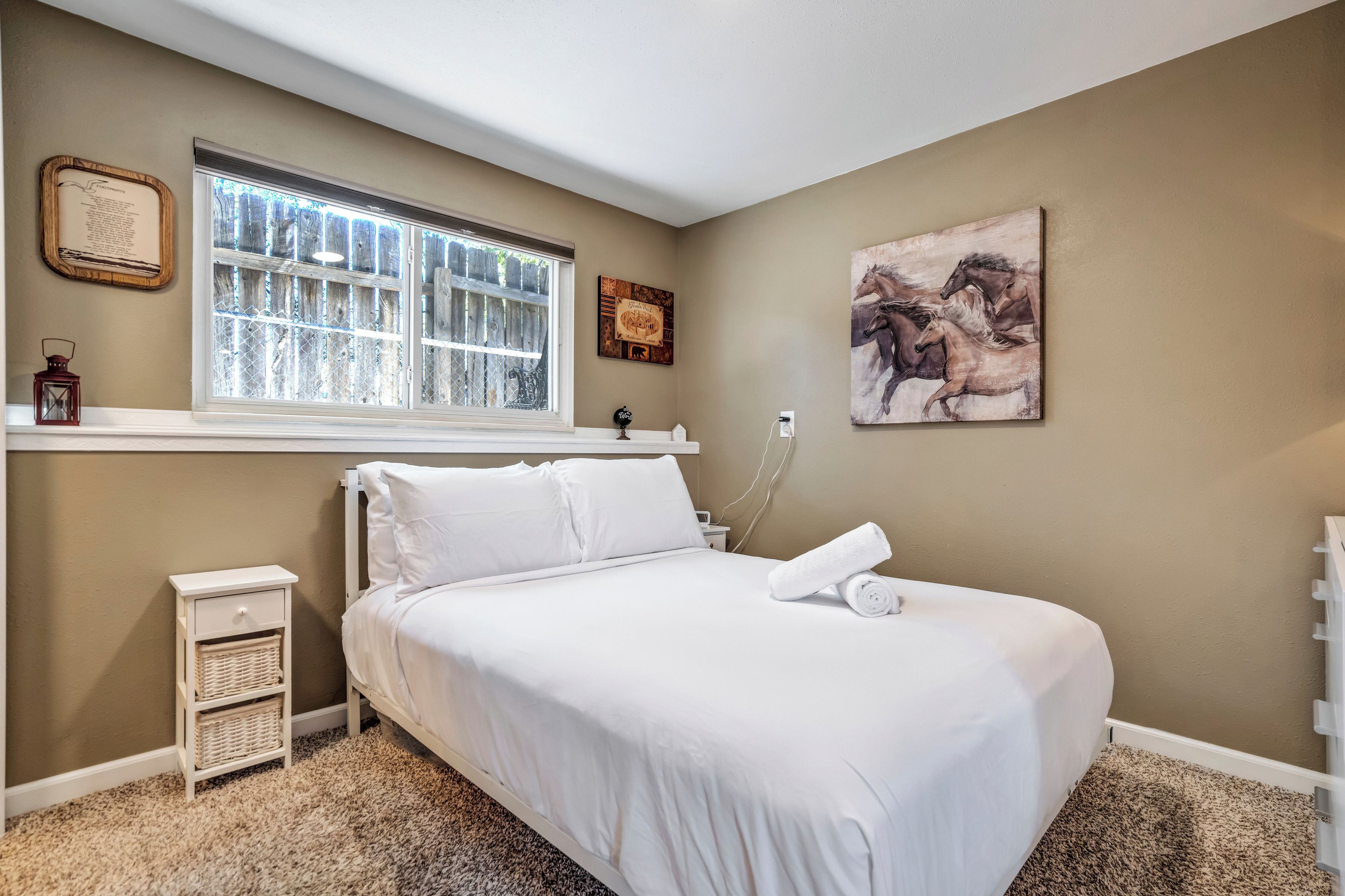 Un dormitorio con cama, mesita de noche, lámpara, ventana con vistas y un cuadro en la pared.