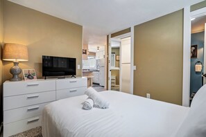 A hotel room with a bed, a television, a desk with a lamp, and a bathroom visible through an open door. - Cozy Garden Retreat | Pet Friendly w/ Private Yard (Colorado Springs)