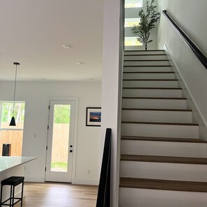 Ein modernes Interieur mit Treppe, einer zur Außenbereits führenden Tür und einer Pendelleuchte.