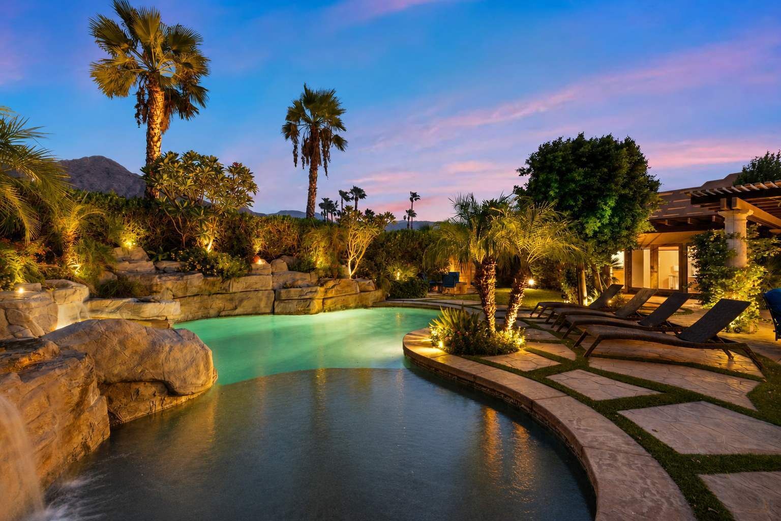 A swimming pool with a curved edge, surrounded by palm trees and a stone wall.