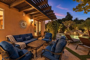 Eine Terrasse im Freien mit einem blauen Sofa, Korbstühlen und einem Poolbereich.