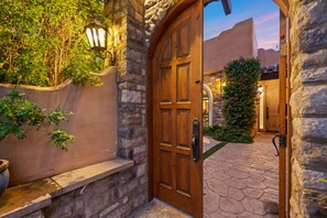 A stone-walled entrance with a wooden door, a lantern, and a pathway leading to a building. - Nightingale by Nest Villas | Lush La Quinta Oasis (La Quinta)