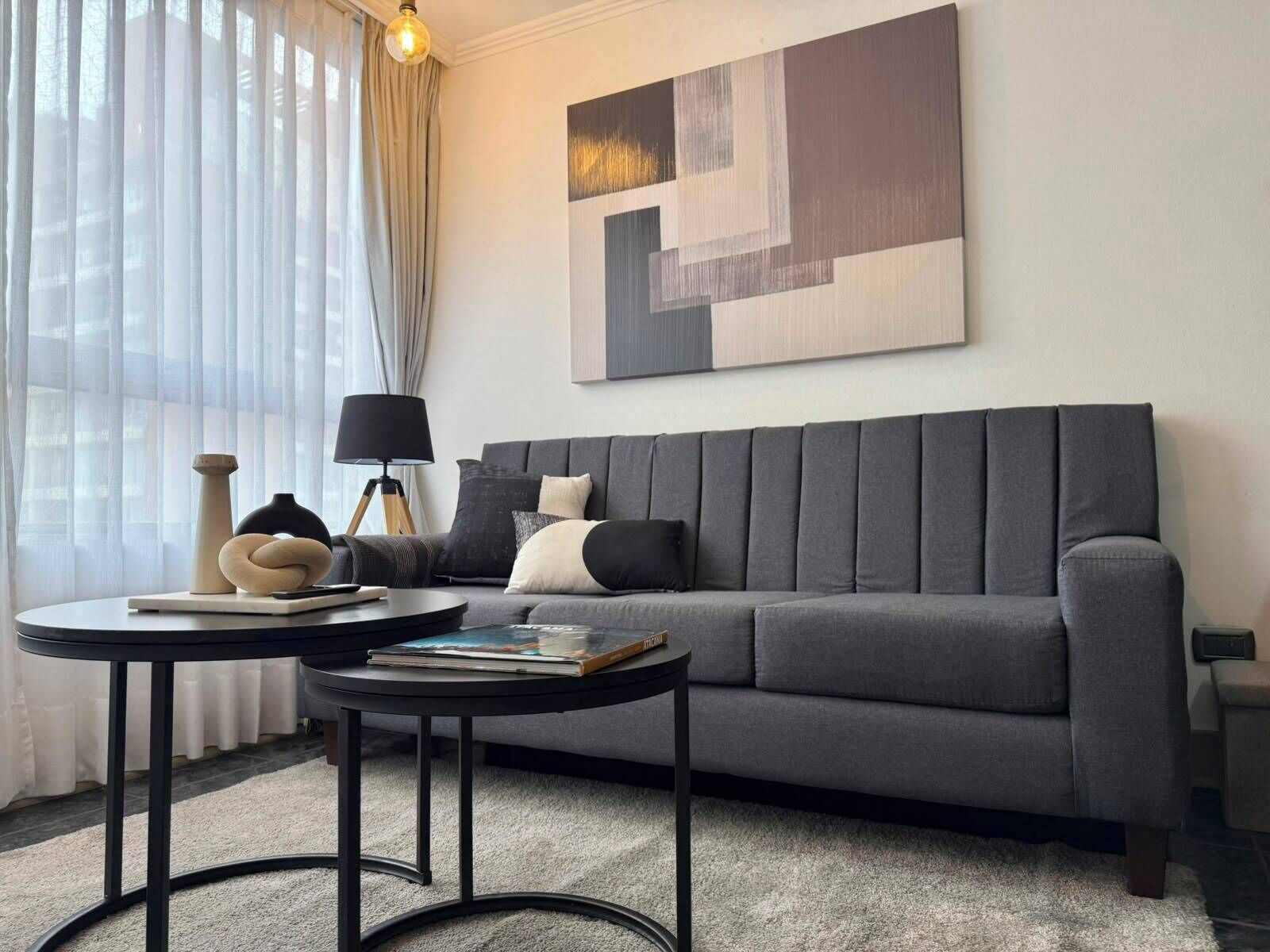 A modern living room with a grey sofa, two black side tables, and a large abstract painting on the wall.