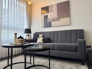 Ein modernes Wohnzimmer mit einem grauen Sofa, zwei schwarzen Beistelltischen und einem großen abstrakten Gemälde an der Wand.