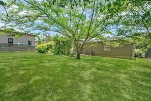 A backyard with a lawn, a tree, a wooden fence, and a building with a window. - The Nest | Charming 2BR Fredericksburg home with grill, full kitchen, and washer/dryer (Fredericksburg)