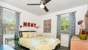 Una camera da letto con un letto, una scrivania, una sedia, una ventola a soffitto e una parete con il cartello 'NEST'.