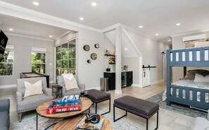A modern living room with a sofa, ottomans, a coffee table, and a bunk bed. - Rio Ranchito | 3BR, 3BA river retreat with hot tub and fire pit (Stonewall)
