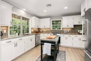 A modern kitchen with white cabinetry, a central island, and a view of greenery through large windows.