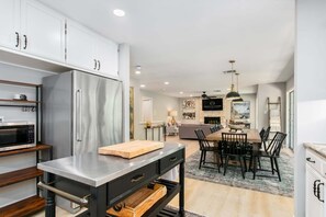 A modern kitchen with a built-in refrigerator, a wooden cutting board, and a dining area with a table and chairs. - Rio Ranchito | 3BR, 3BA river retreat with hot tub and fire pit (Stonewall)
