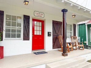 Una cabaña con puerta roja, un letrero que dice 'Cotton Mill Cottage' y un porche con mecedoras.