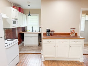 A kitchen with white cabinets, a microwave, a stove, a sink, and a coffee maker.
