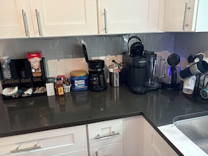 A kitchen counter with various coffee and tea products, including a Keurig coffee maker, a Maxwell House coffee jar, and a coffee and tea dispenser. - Cozy 2-bedroom bungalow in East Nashville (Nashville)