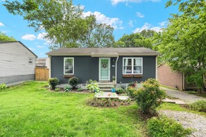 A two-story house with a front porch, a green door, and a small garden with various plants and flowers. - Cozy 2-bedroom bungalow in East Nashville (Nashville)