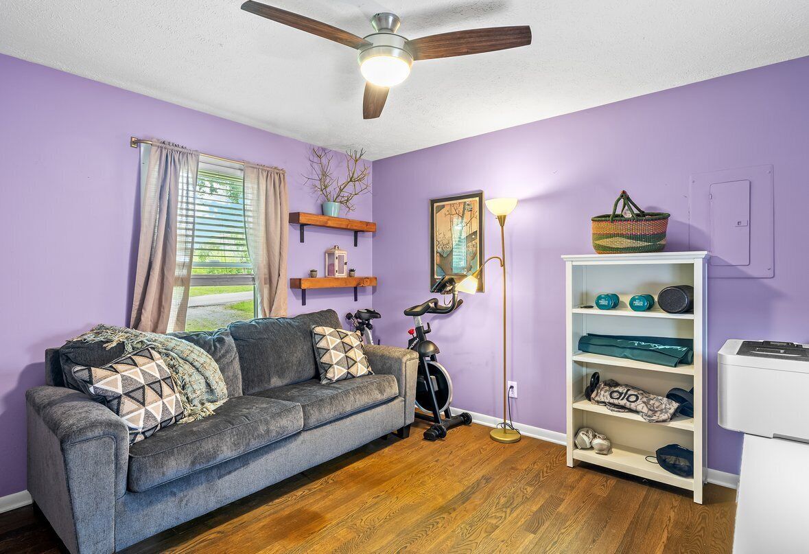 A room with a grey sofa, a ceiling fan, a standing lamp, and a white shelf with shoes.