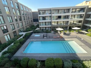 A rooftop swimming pool with a wooden deck, surrounded by greenery and modern buildings. - Quiet Studio, Best Price, and Near the Metro (Santiago)