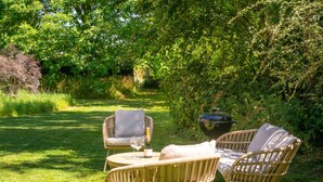 Un espace extérieur aménagé avec des chaises et une table en osier, entouré d’une végétation luxuriante.