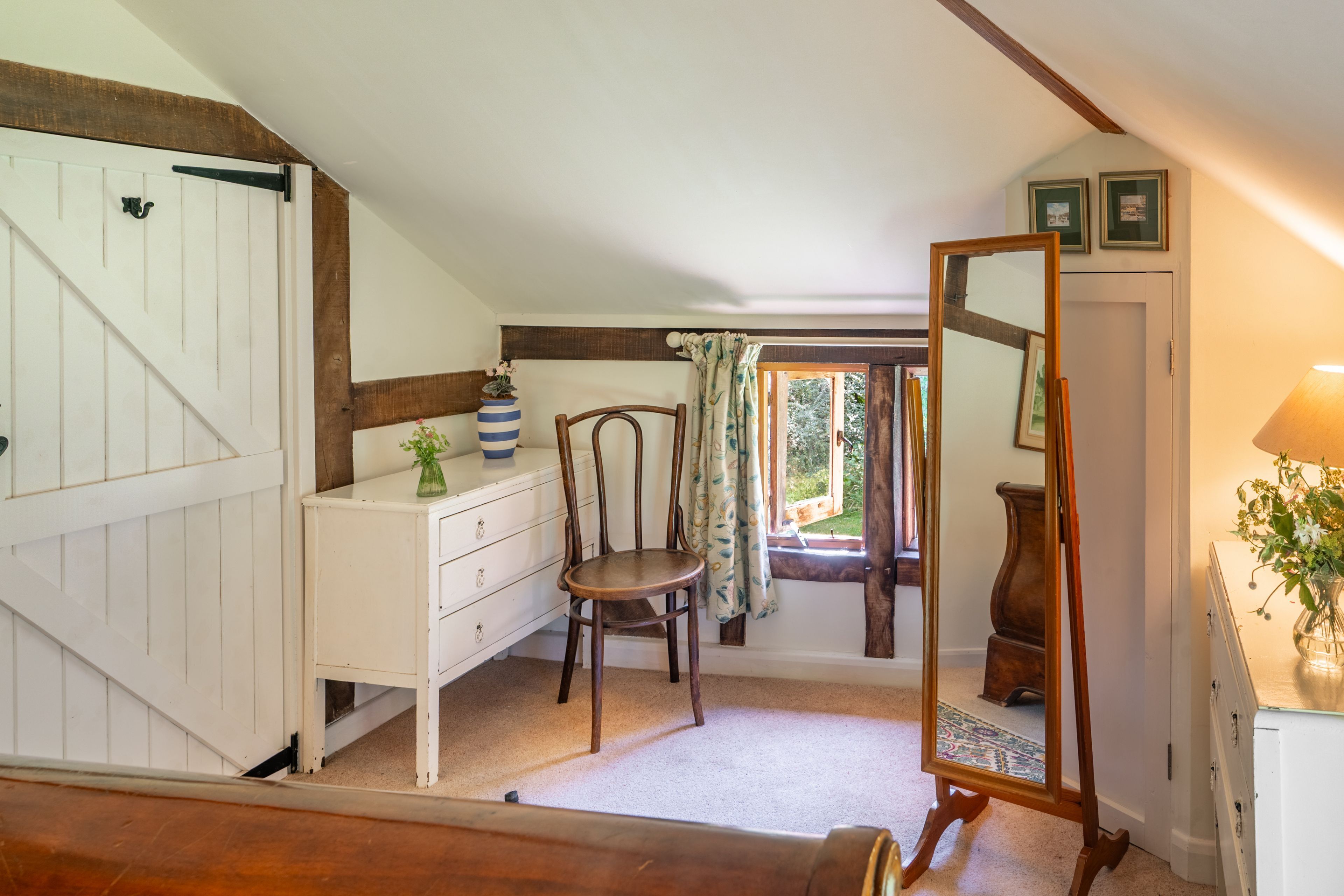 Una habitación con un aparador blanco, una silla de madera, un espejo y una ventana con cortinas.
