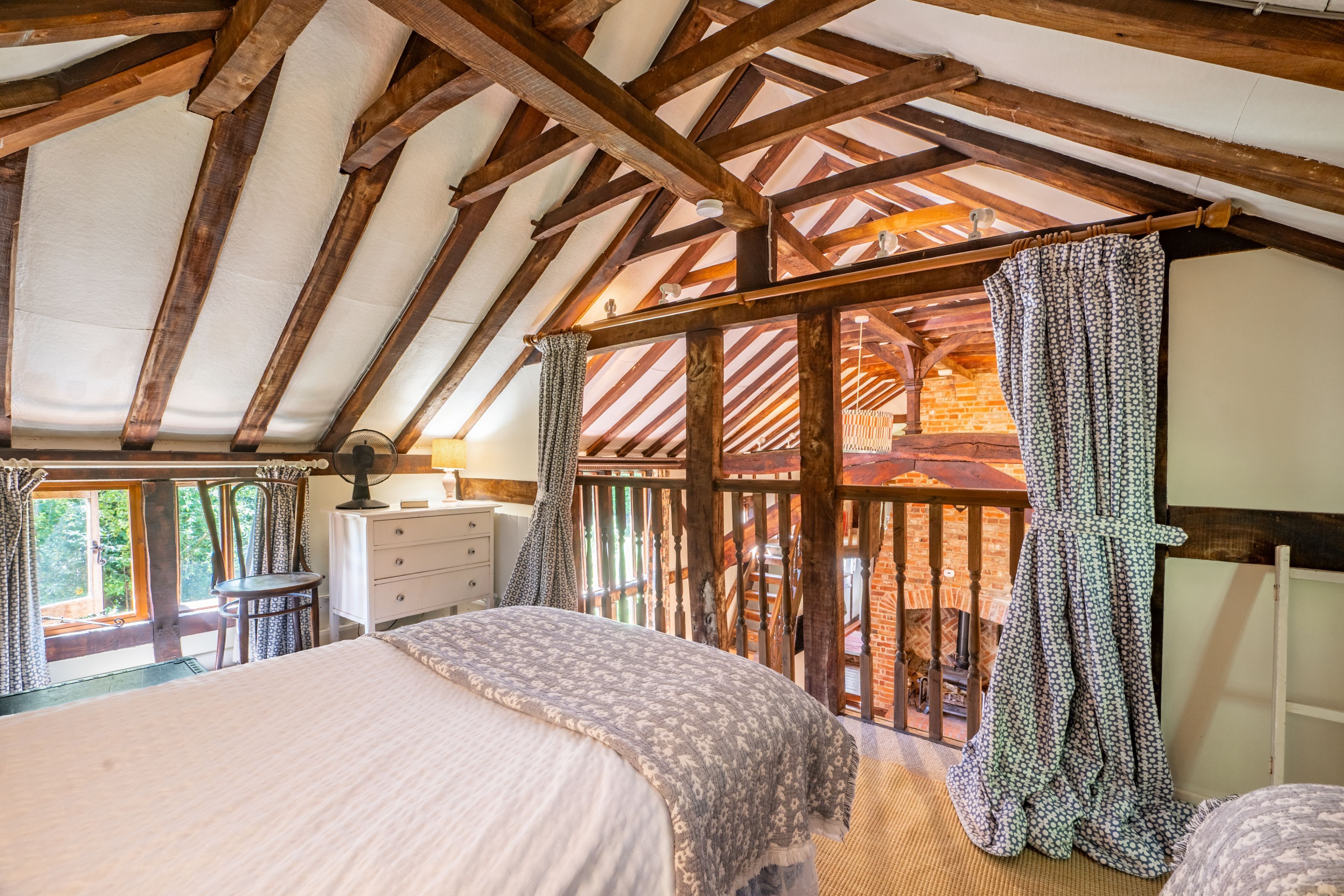 A bedroom with a wooden ceiling, a bed, a dresser, and a window with curtains.
